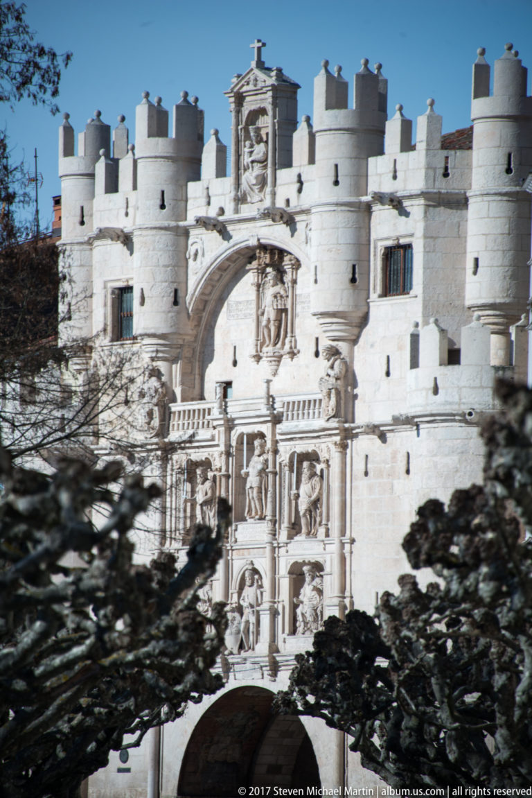 White-stone Arco de Santa María with crenellated towers, monumental arch, sculpted niches, and heraldic decoration.