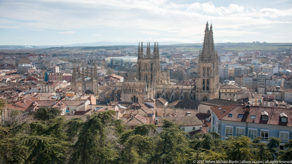 Wide hillside panorama of Burgos with the cathedral’s twin spires rising above red roofs and the surrounding city.