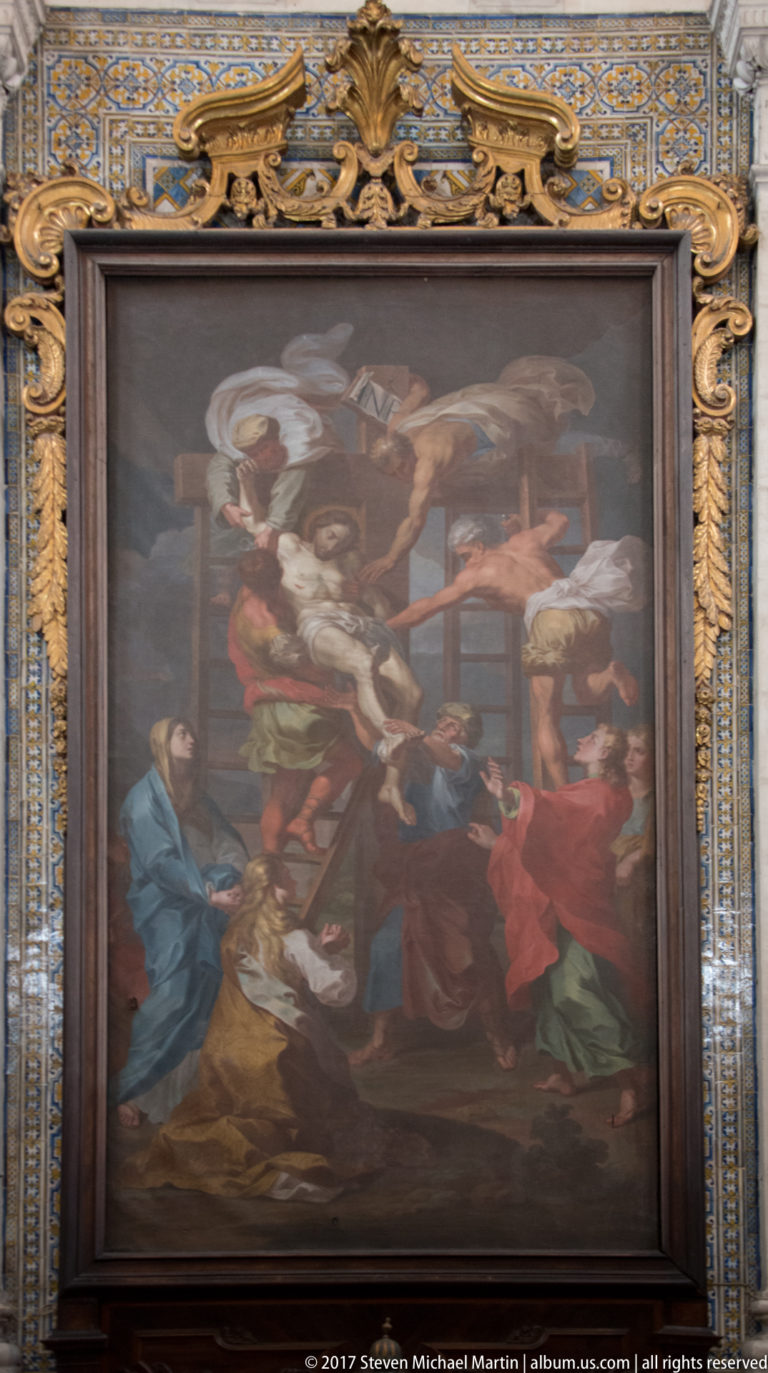 Large gilded religious painting with many figures in vivid robes, mounted against patterned blue-and-gold tiles.