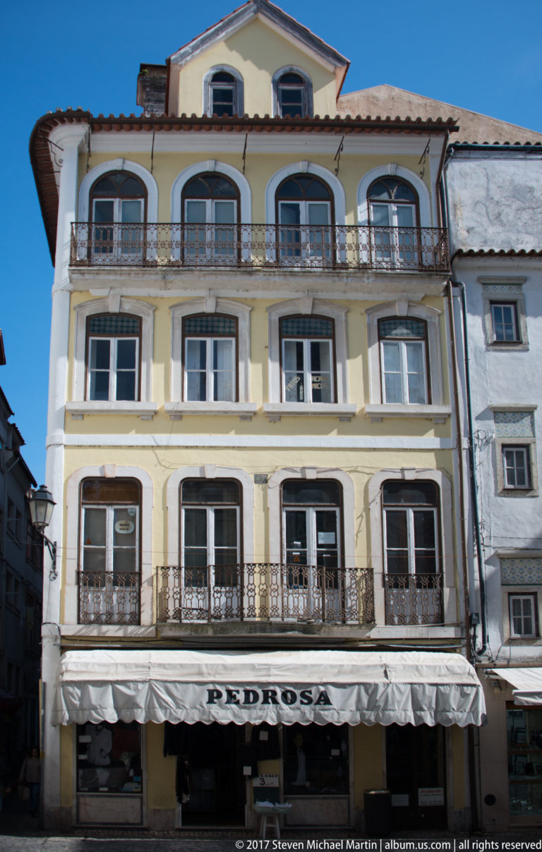 Tall pale building with iron balconies and a Pedrosa storefront beneath a striped awning.