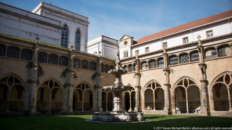 Stone cloister with pointed arches surrounding a green courtyard and central fountain at Santa Cruz Monastery.