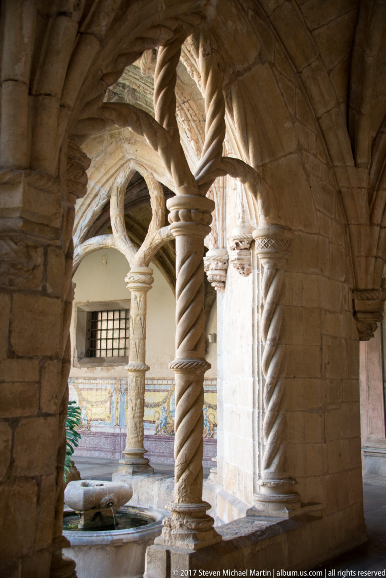 Twisted stone columns and interlacing arches framing a small cloister courtyard and basin.