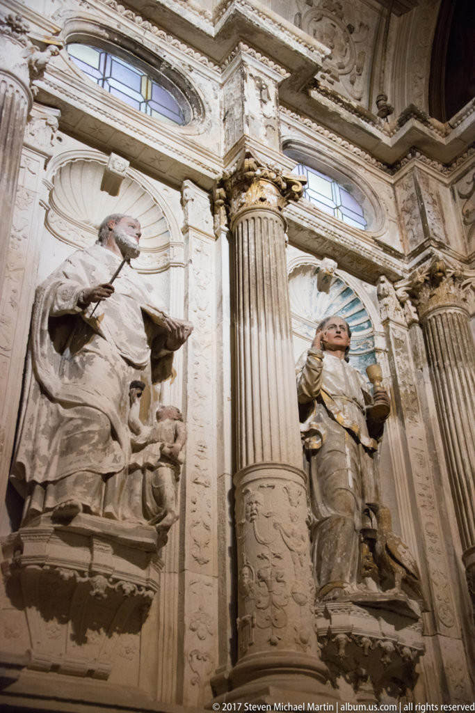 Low-angle view of large pale stone figures in carved niches between fluted columns inside a church.