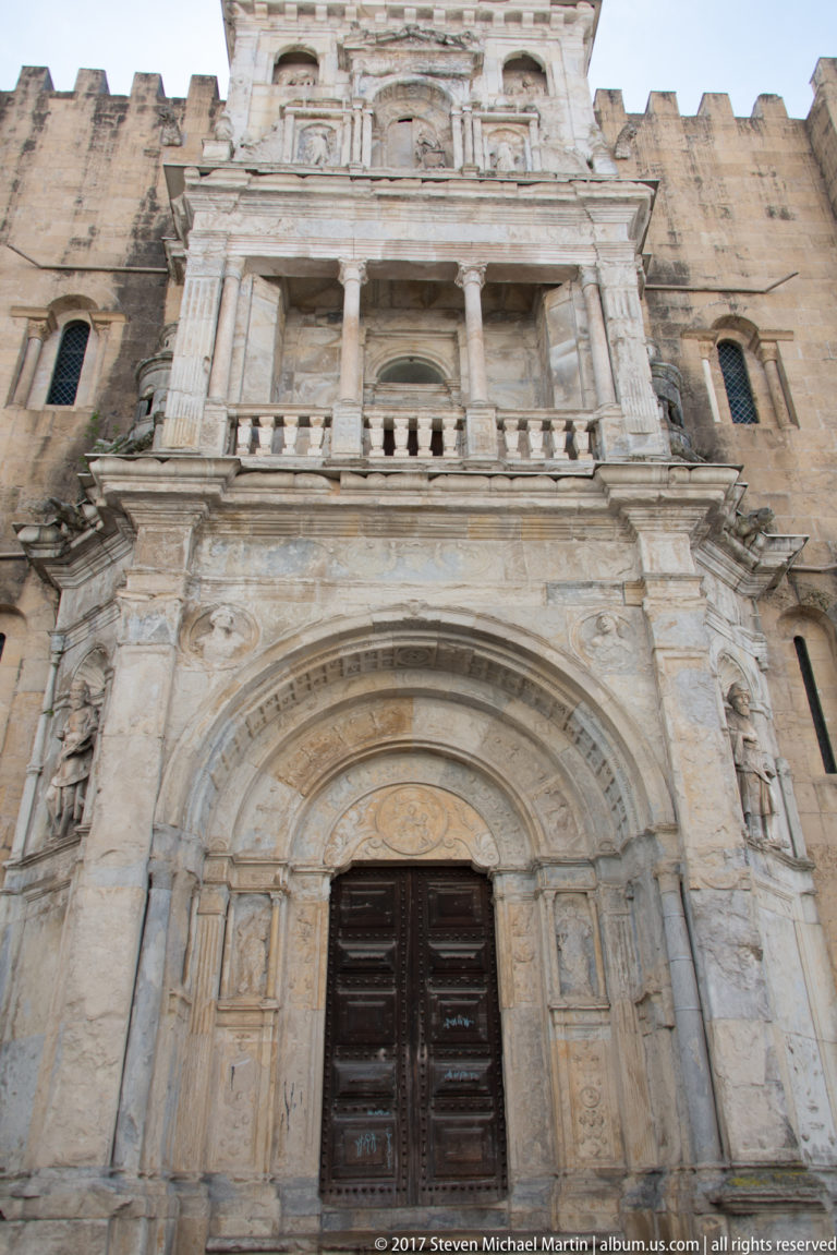 Elaborate three-level Renaissance Porta Especiosa with carved columns, niches, balustrade, and wooden doorway on Coimbra’s Old Cathedral.