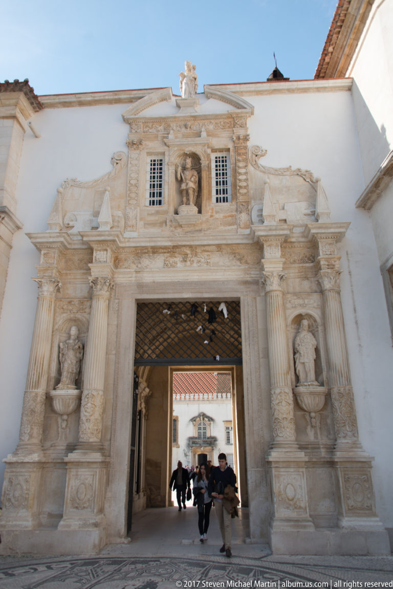 Ornate stone Porta Férrea with columns, statues, heraldic carving, and a broad passage opening into the University of Coimbra.
