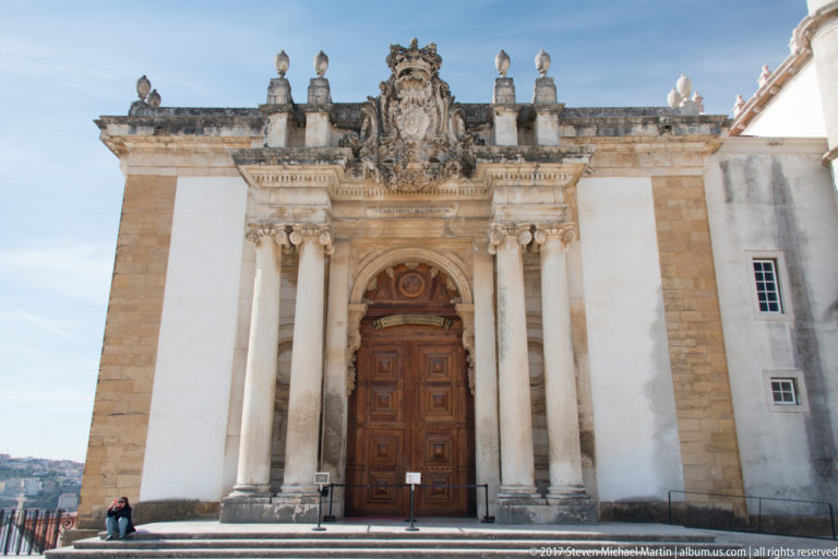 Baroque stone portal of the Joanina Library with paired columns, royal crest, sculpted pediment, and a tall paneled wooden door.