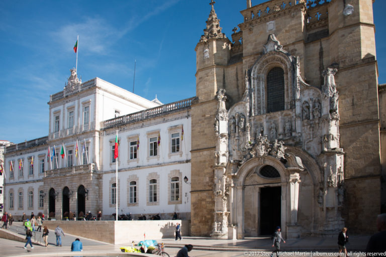 Ornate stone façade of Santa Cruz Church beside the white Coimbra City Hall on a sunlit square.