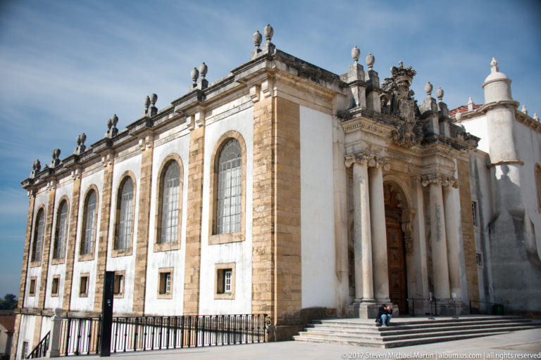Oblique exterior of the Joanina Library with tall arched windows, pale stone walls, and an ornate columned entrance bay.
