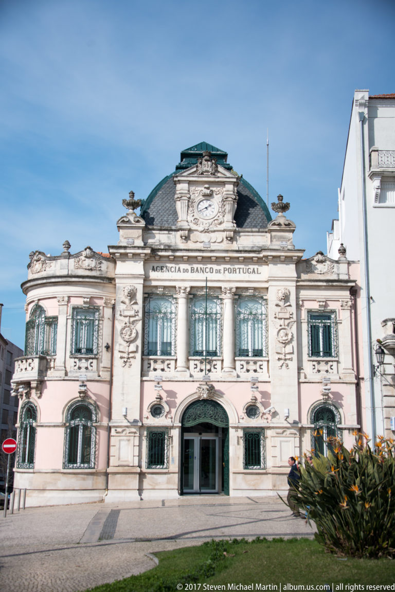 Ornate former Banco de Portugal façade with arched windows, sculpted stonework, central entrance, and the bank inscription above.