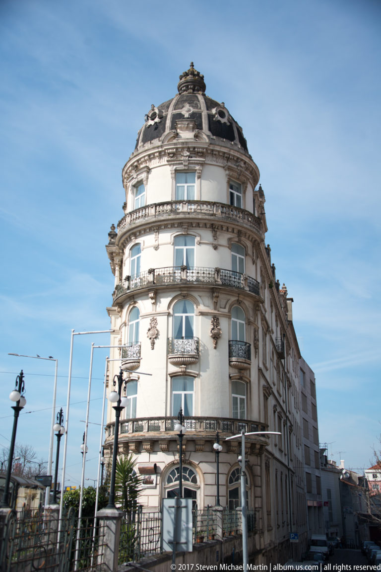 Rounded corner façade of Hotel Astória with curved balconies, arched windows, ornate stonework, and a dark domed roof.