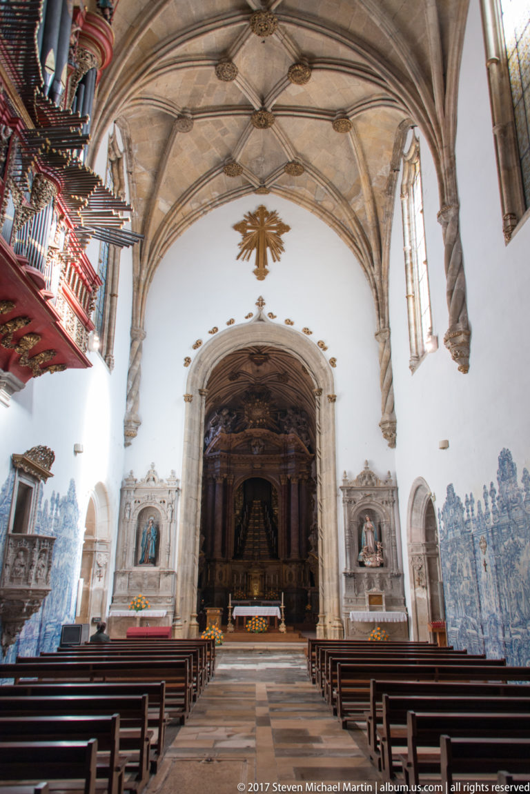 Central aisle and pews beneath ribbed vaulting in Santa Cruz Church, with blue-and-white tiled walls.