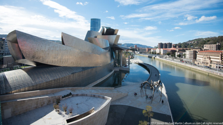 High view along the Guggenheim Museum Bilbao and river, with Maman on the terrace and city buildings extending downstream.