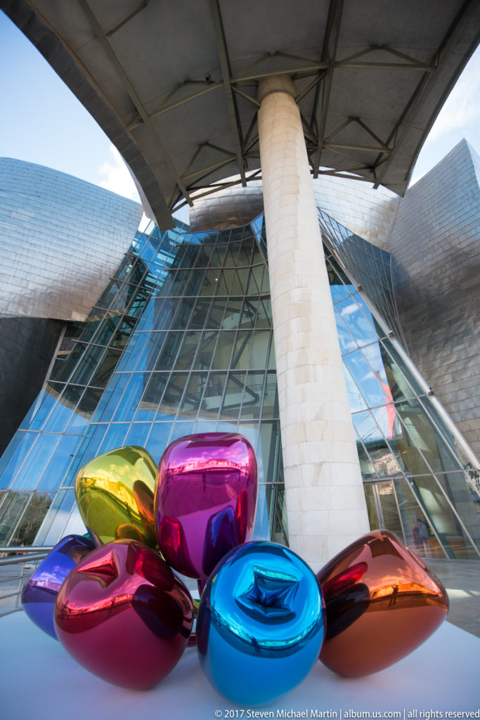 Close view of multicolored mirrored forms of Jeff Koons’s Tulips with the Guggenheim Museum Bilbao façade behind.