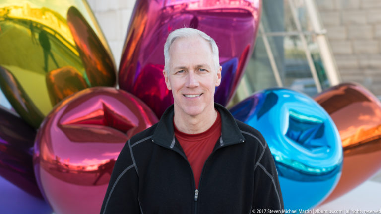 Man standing before the multicolored reflective Tulips sculpture by Jeff Koons at the Guggenheim Museum Bilbao.