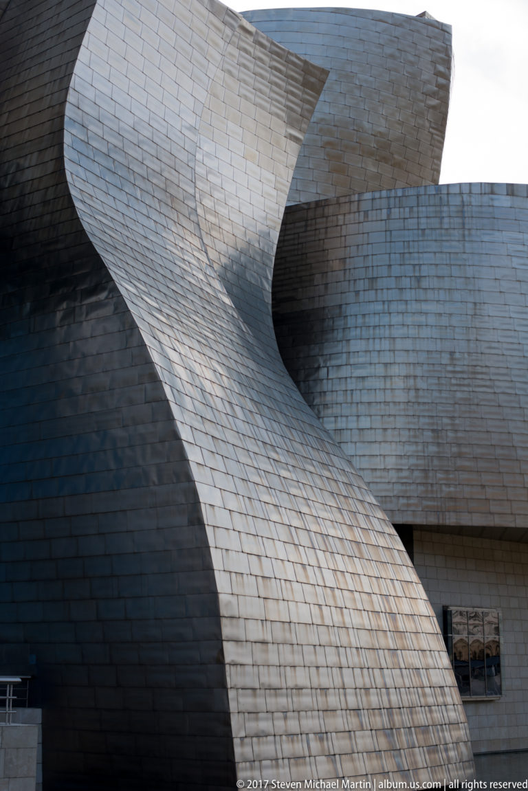 Close architectural view of overlapping curved titanium-clad walls and a shadowed recess on the Guggenheim Museum Bilbao exterior.
