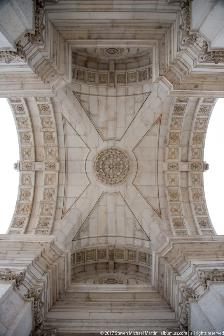 Symmetrical upward view of the Rua Augusta Arch vault with star-shaped stone geometry and circular central boss.