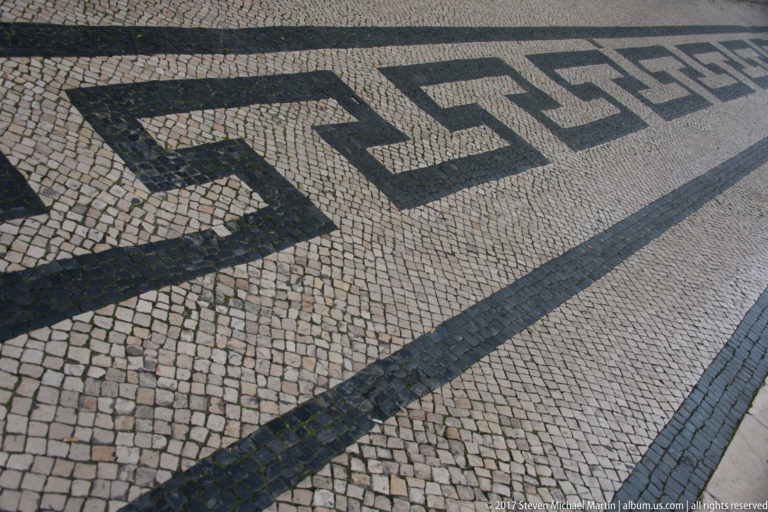 Close oblique view of black-and-white Portuguese mosaic pavement arranged in a bold interlocking geometric pattern.