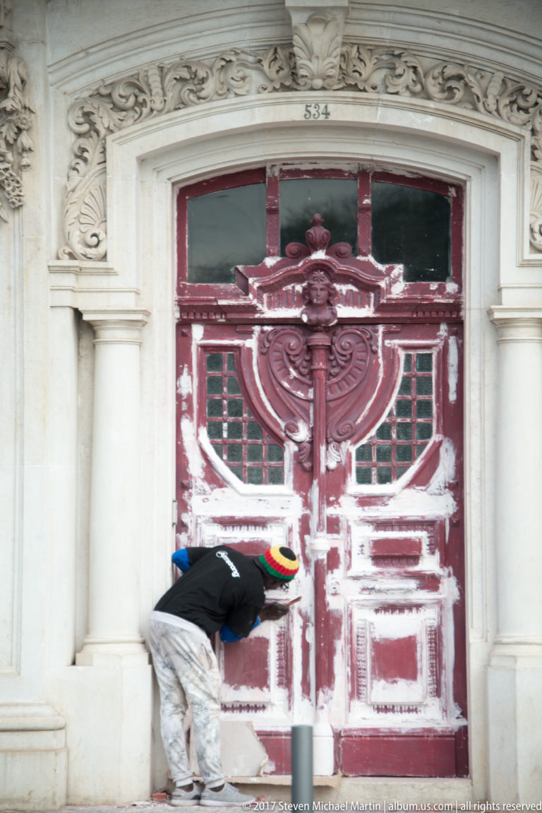 Weathered red double doors with large heraldic motif in an ornate stone surround dated 1834, with a worker below.