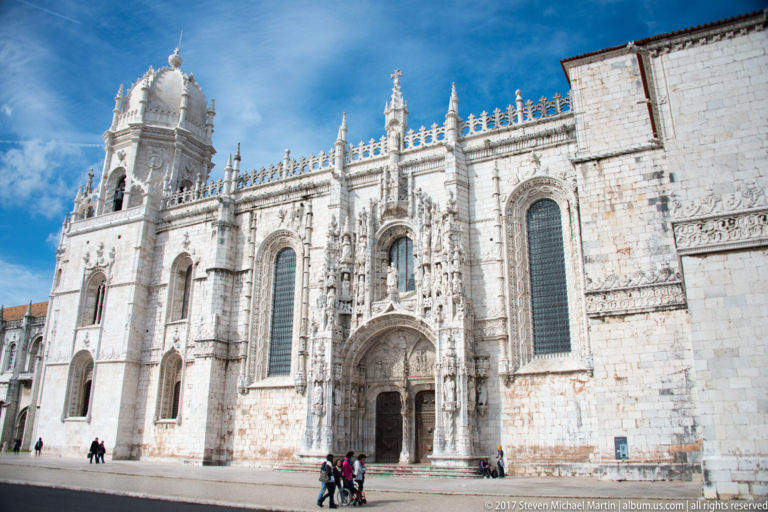 South façade of the Jerónimos Monastery church with tall windows, pinnacles, and richly carved Manueline portal.
