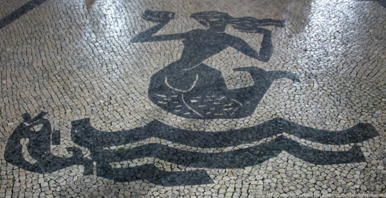 Black-and-white Portuguese pavement mosaic showing a stylized sea creature above several wavy bands.