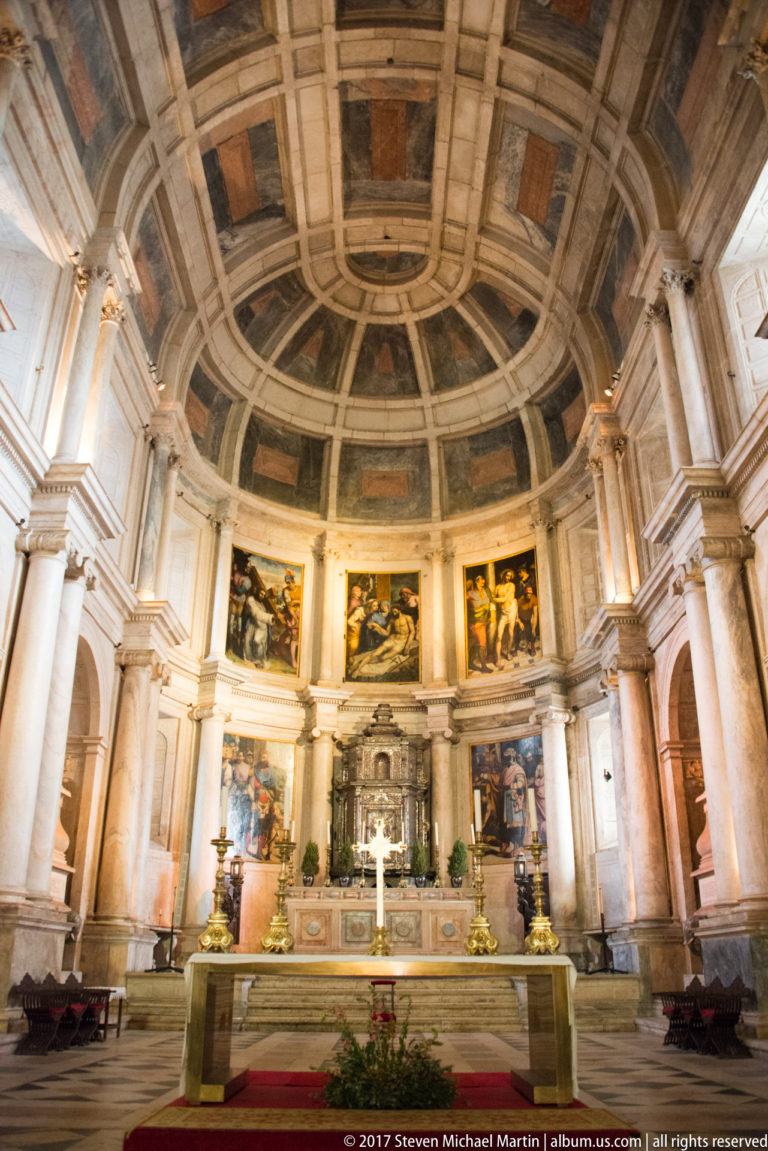 Main chapel altar at Jerónimos with large religious paintings between pale columns beneath a curved coffered upper wall.