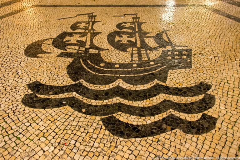 Black-and-white Portuguese pavement mosaic depicting a multi-masted sailing ship riding over stylized waves.
