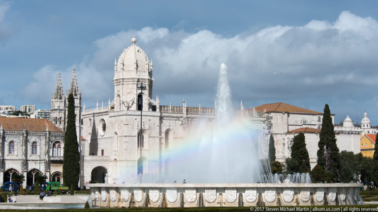 Fountain spray and rainbow in Praça do Império with the towers of the Jerónimos Monastery behind.