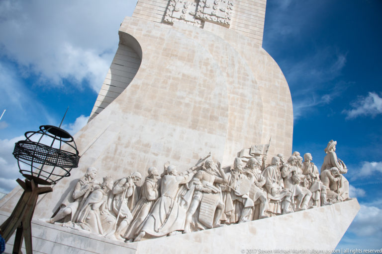 Low-angle view of the Monument to the Discoveries with a procession of carved historical figures along its sloping side.