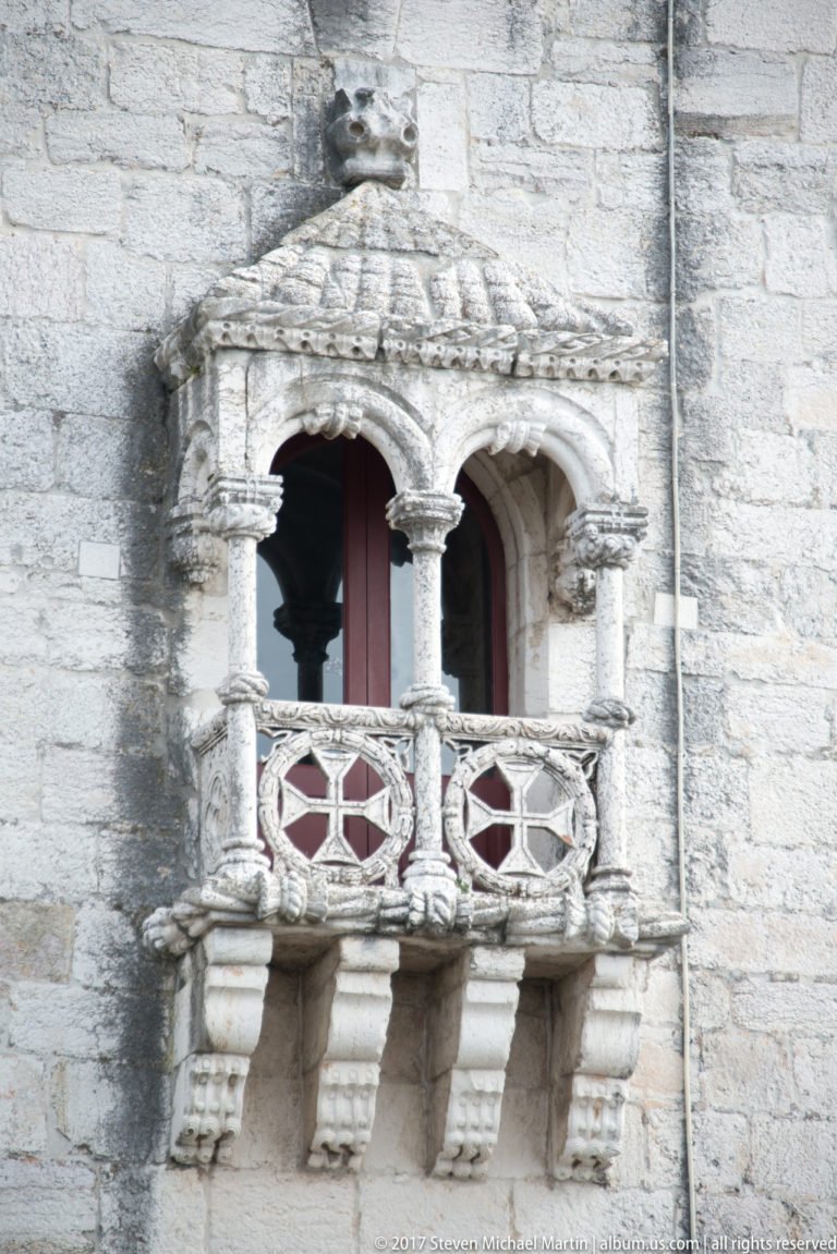 Projecting carved stone balcony on Belém Tower with twisted columns, openwork roundels, shell canopy, and sculpted brackets.