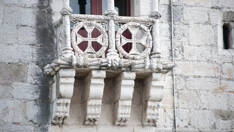 Close view of Belém Tower balcony parapet with circular openwork panels, rope-like carving, clustered columns, and sculpted brackets.