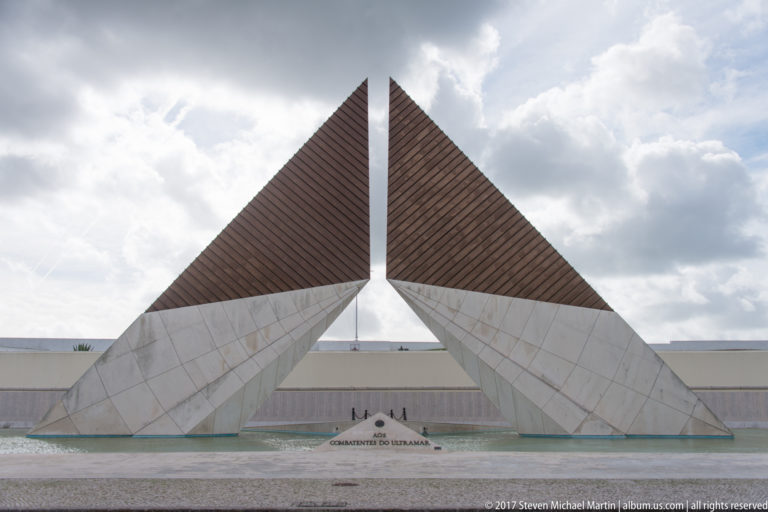 Two triangular stone pylons rising above a reflecting pool at the Monument to the Overseas Combatants in Belém.