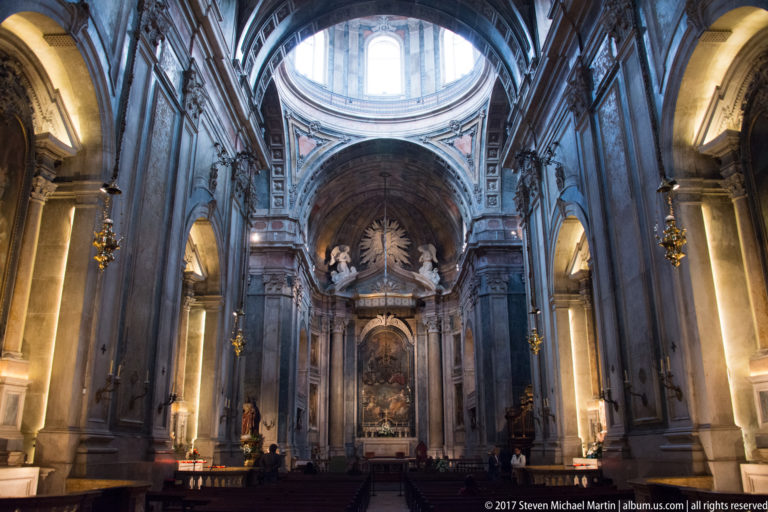 Wide interior of the Basílica da Estrela showing marble piers, side arches, dome, pews, and the main chapel ahead.