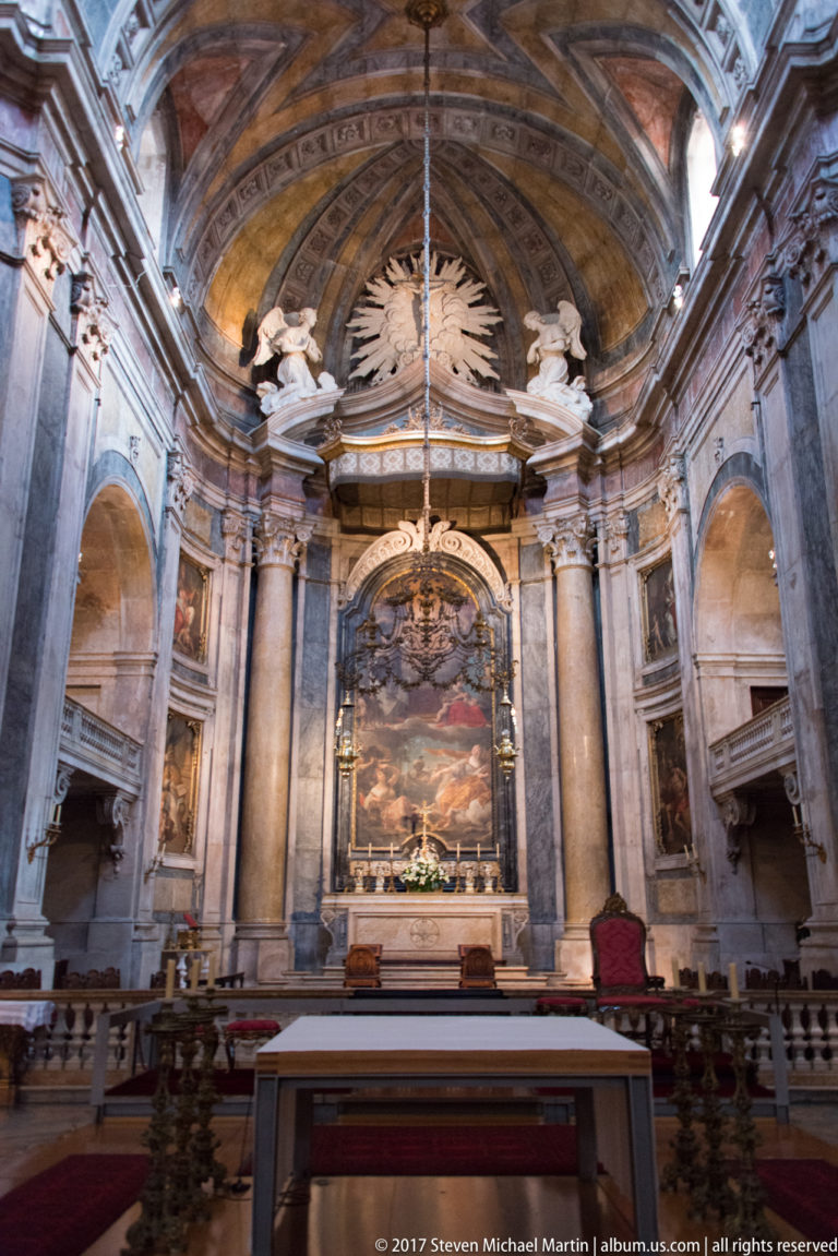 High altar in the Basílica da Estrela framed by marble columns, sculpted angels, radiant ornament, and a large religious painting.