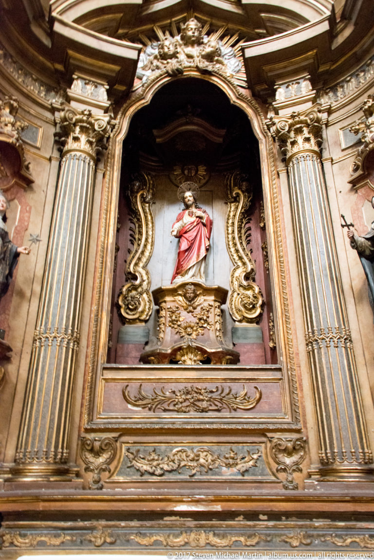 Gilded church side altar with fluted columns, carved scrollwork, and a polychrome statue in a deep niche.