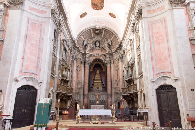 Axial church interior with high altar, decorated apse, pale stone walls, and gilded furnishings along the chancel.
