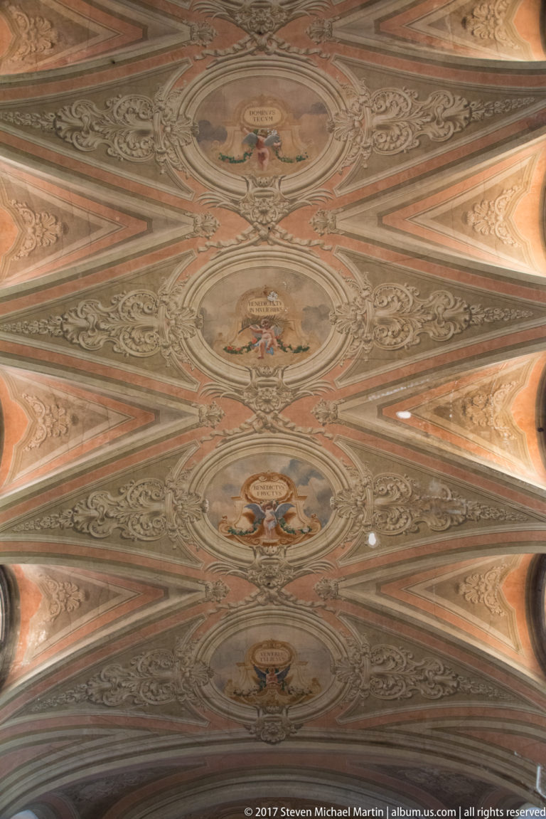 Ornamental church ceiling divided into geometric panels with scrollwork and small painted figurative medallions.