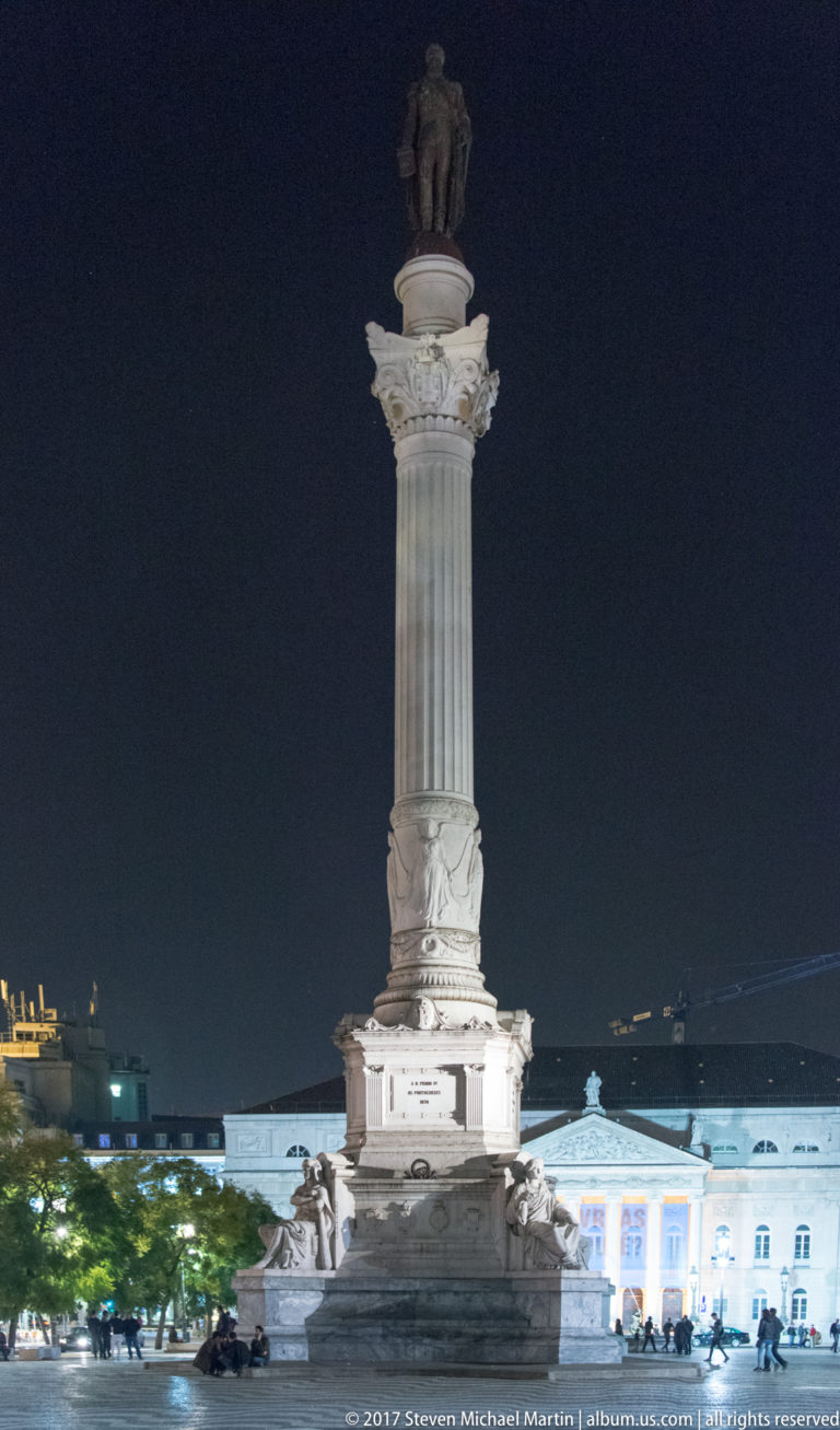 Illuminated Monument to Pedro IV, with a tall fluted column and standing statue, rising against the night sky.