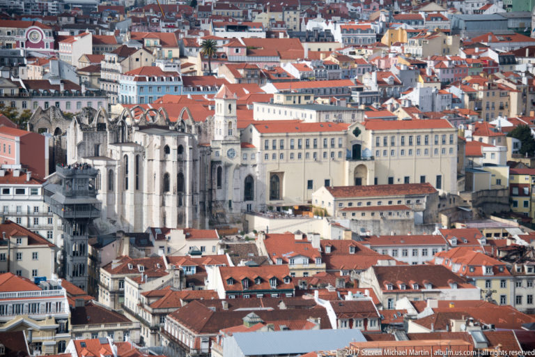 Roofless Gothic Carmo Convent rising above dense red-tiled buildings in central Lisbon.
