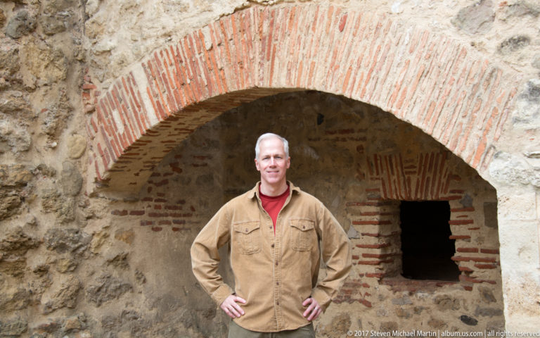 Man standing beneath a broad brick-lined arch in rough stone masonry at São Jorge Castle.