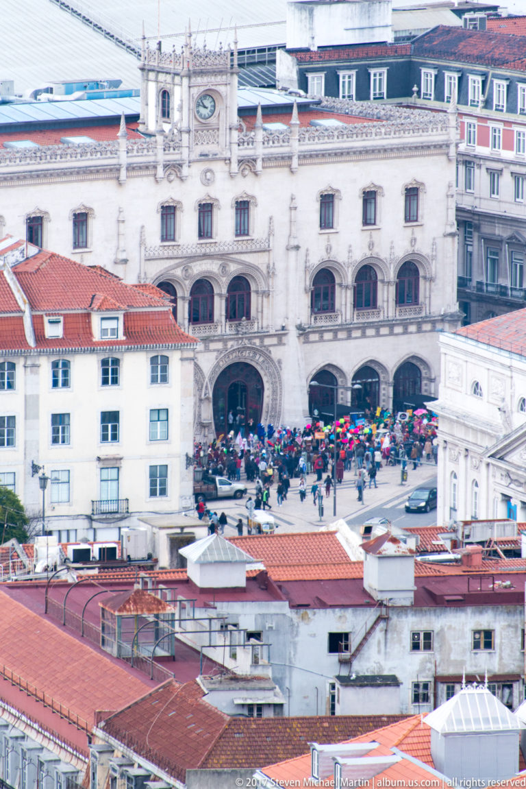 Ornate pale façade of Rossio railway station with paired arched entrances and crowds gathered outside.