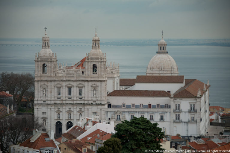 São Vicente de Fora's twin-towered white façade with the National Pantheon dome behind and the Tagus in the distance.