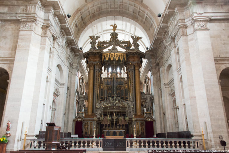 Elaborate dark wood and gilded high altar of São Vicente de Fora beneath a tall stone arch.