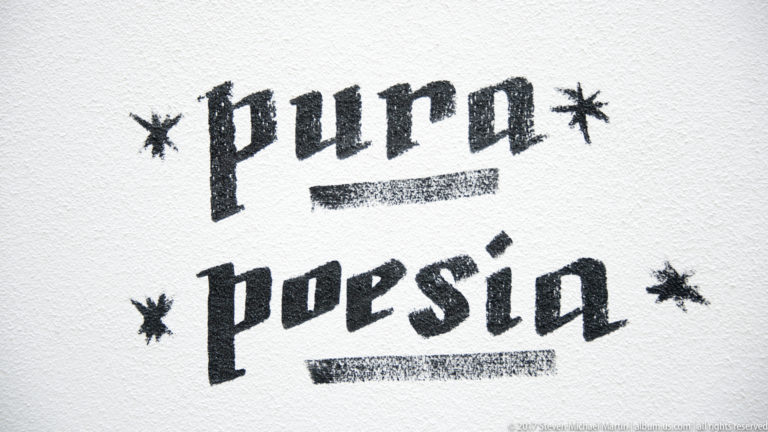 Black stencil text 'pura poesia' with stars and underlines on a white wall.