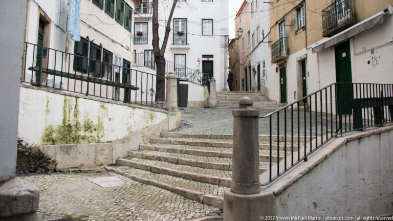 Stone steps climbing between weathered residential façades with railings, doors, and cobbled paving.