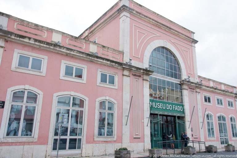 Pink Museu do Fado façade with tall arched central window and green entrance sign.