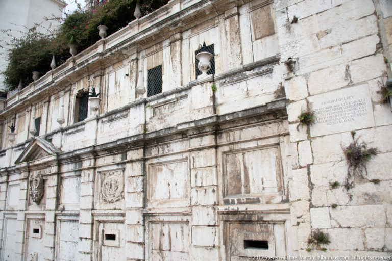 Weathered stone façade of Chafariz d'El-Rei with relief panels, lamps, outlets, and inscription.