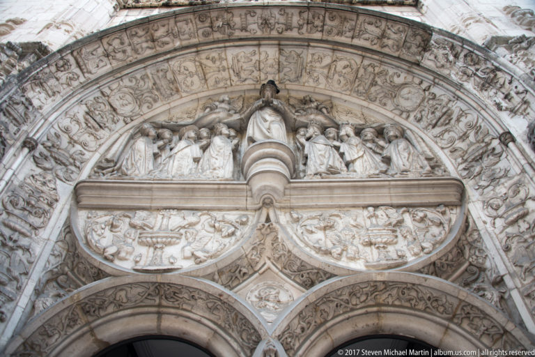 Elaborately carved Manueline church portal with sculpted figures, layered arches, and dense stone ornament.