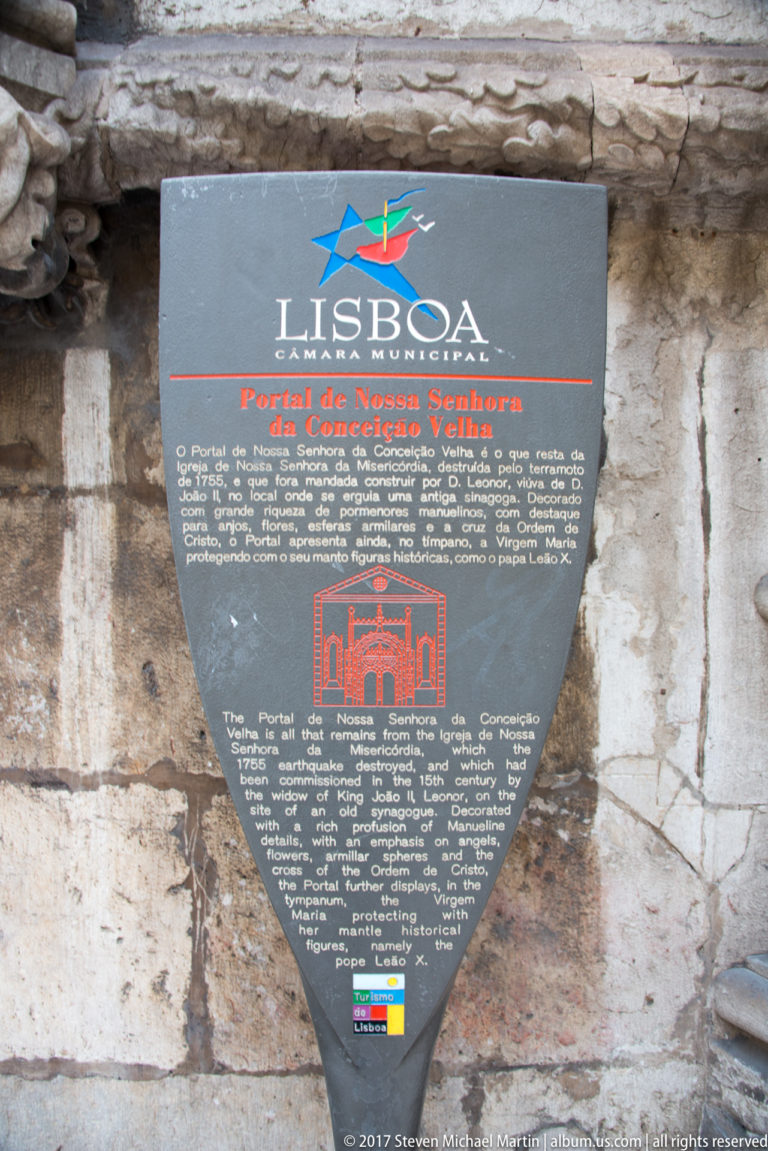 Dark heritage plaque on stone wall titled 'Portal de Nossa Senhora da Conceição Velha' with bilingual text.