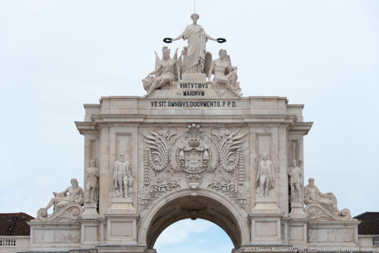 Upper Arco da Rua Augusta with royal arms, carved ornament, Latin inscription, and crowning allegorical figures.