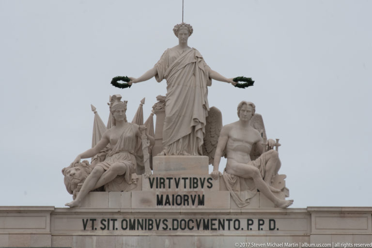 Crowning allegorical group on the Arco da Rua Augusta with standing Glory holding wreaths above two seated figures.